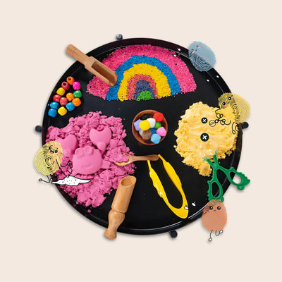 A black sensory play tray filled with colorful sand, beads, and tools for creative play.