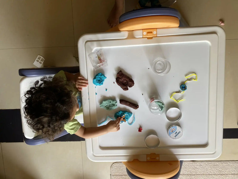 A child engaged in play with colorful modeling clay on a white activity table.