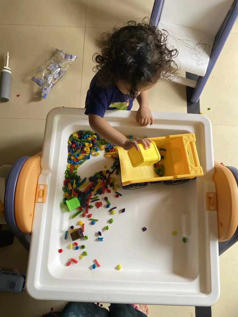 A child’s play table with a large yellow toy truck and colorful building blocks.