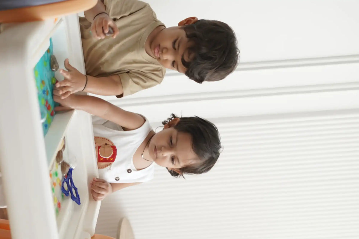 Two young children engaged in sensory play at a dual-basin activity table.