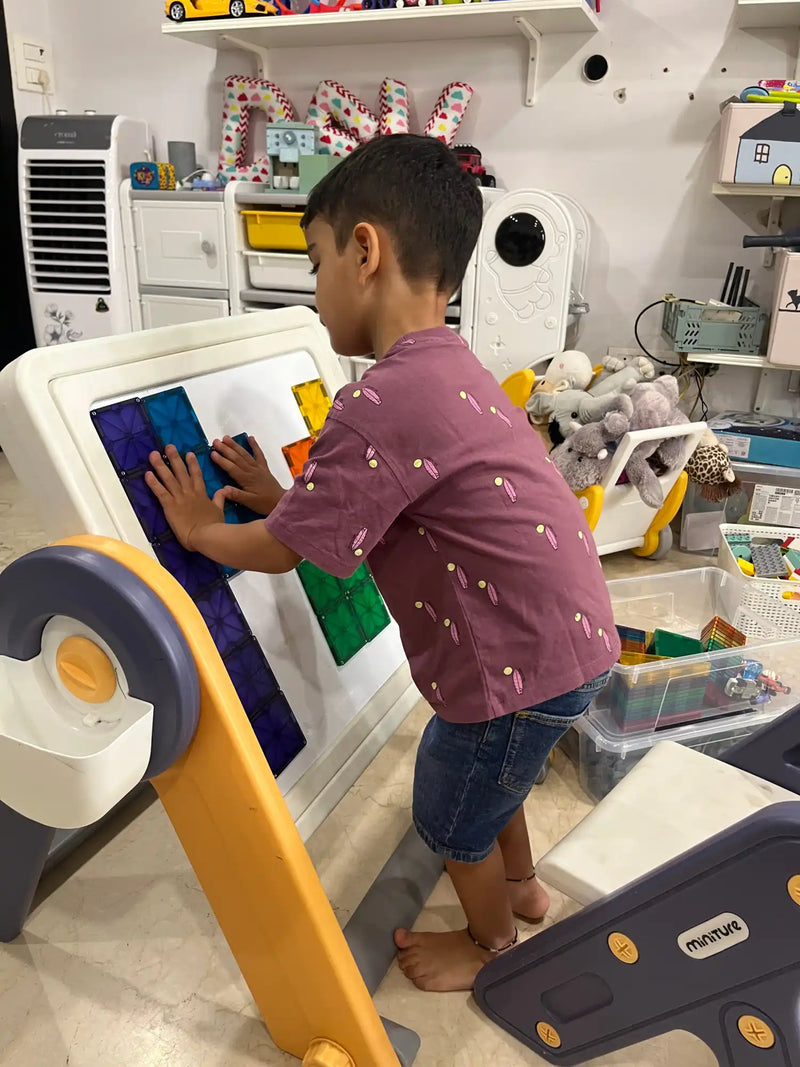 A young boy playing with colorful magnetic tiles on an easel.