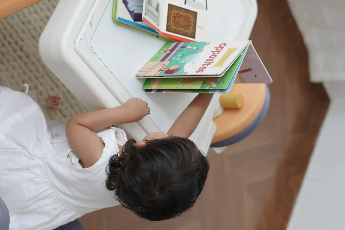 A young child in a white dress interacting with a children’s book titled ’opposites’ on a white table.