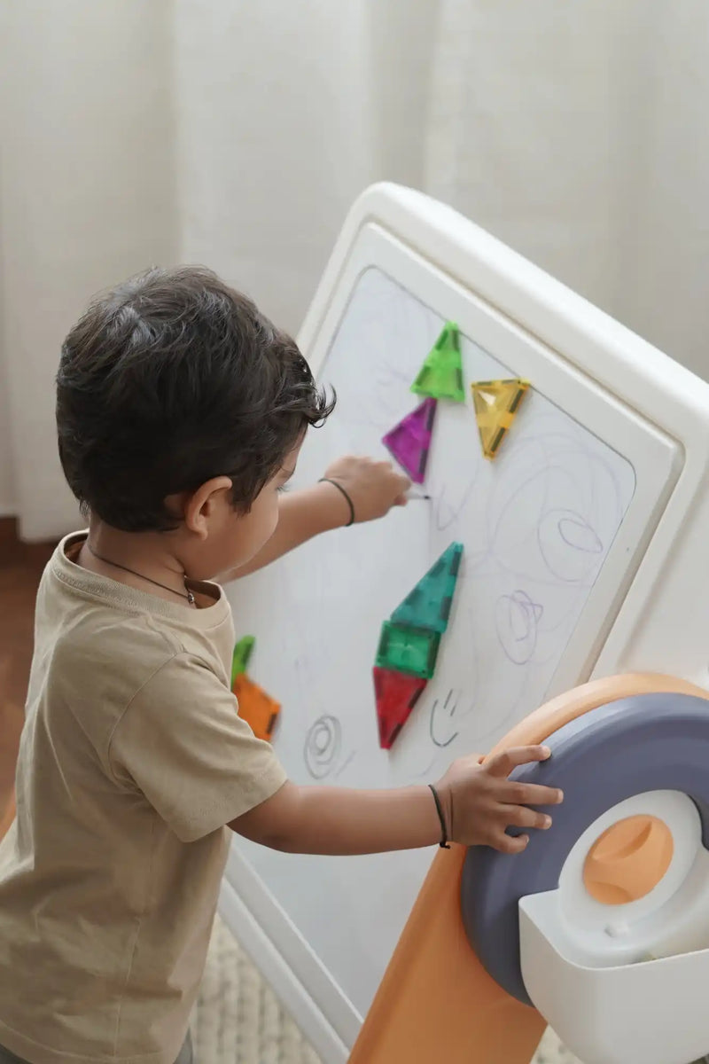 A child playing with colorful magnetic shapes on a white easel.