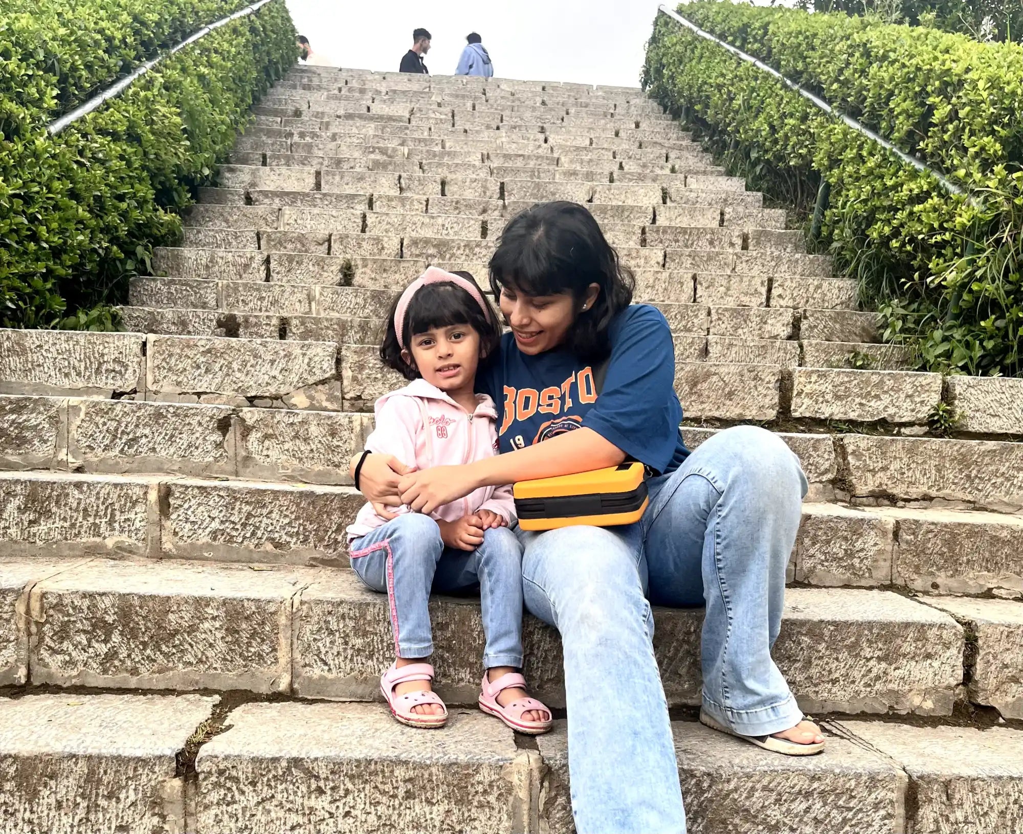 Two people sitting together on concrete steps bordered by green hedges.