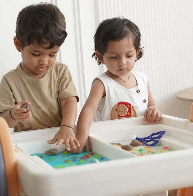 Two young children engaged in sensory play at a dual-basin activity table.