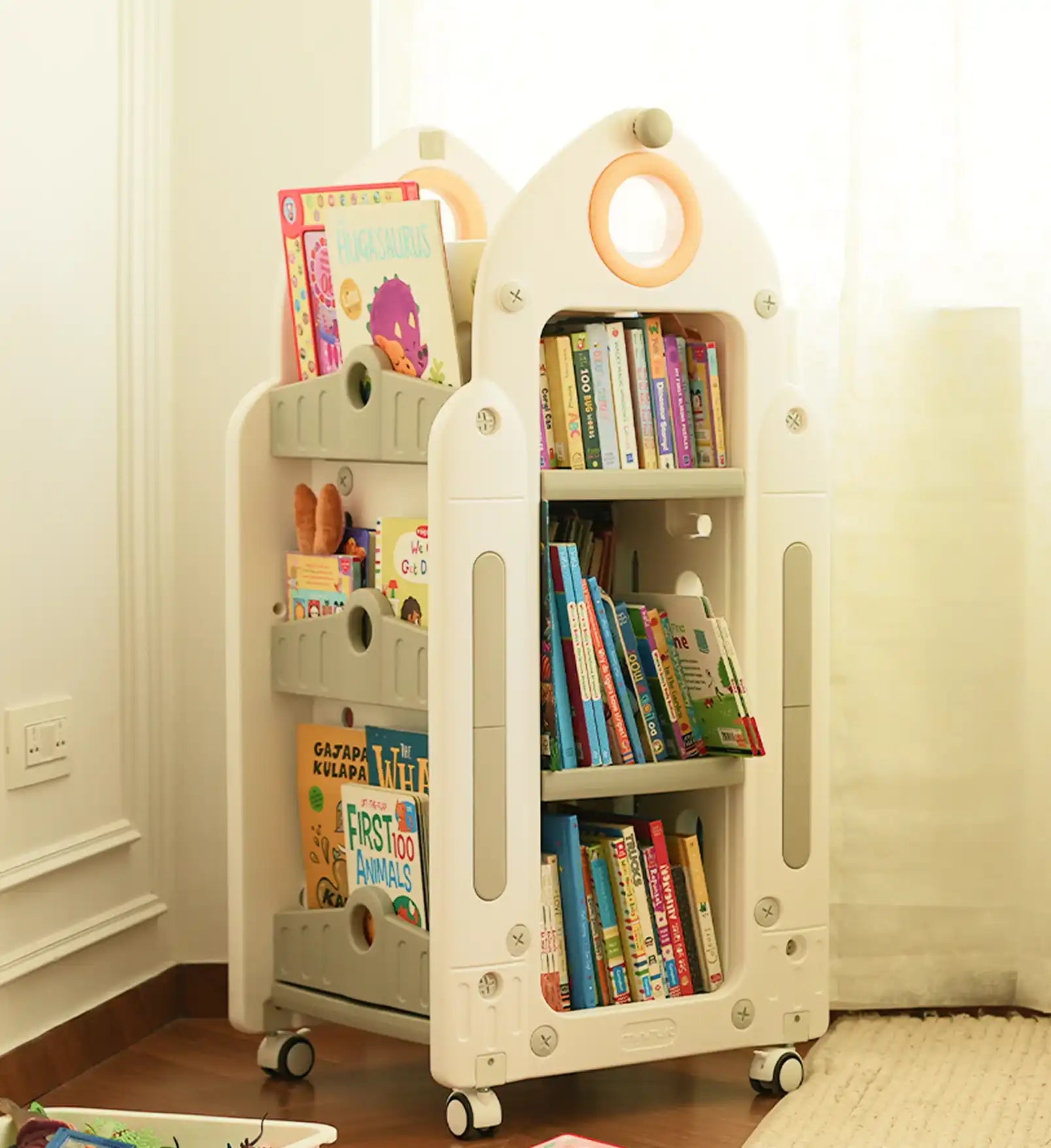 A white and gray children’s rolling bookshelf with multiple shelves and a rocket-ship-like design.